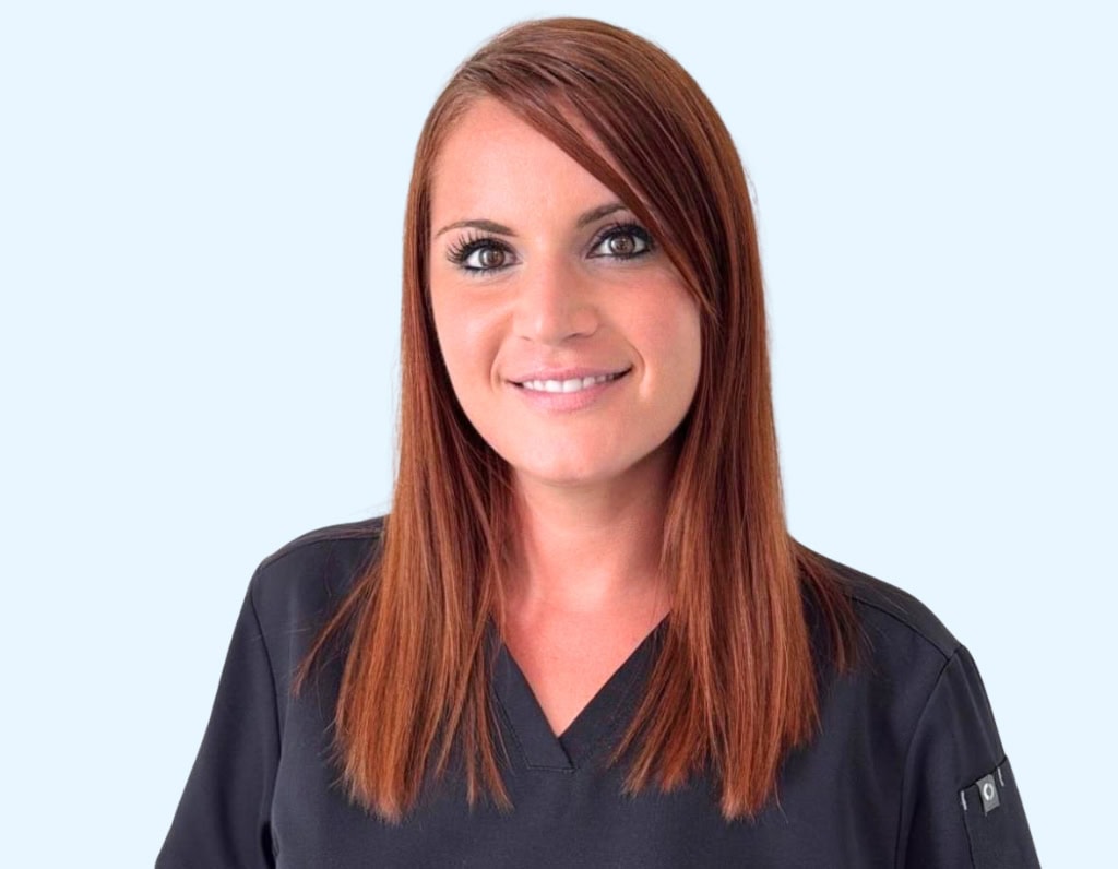 Praticienne dentaire souriante portant une blouse noire, spécialisée en soins dentaires et implants.