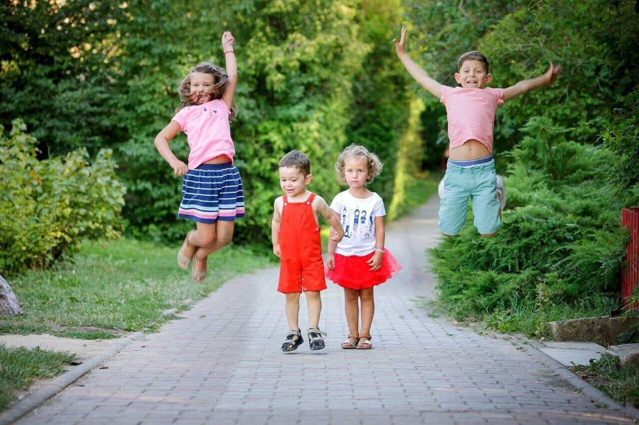 Smiling children jumping and walking in a green park, representing children's oral health and well-being. Photo adapted to illustrate Dental Swiss Clinics' pediatric and dental services. 